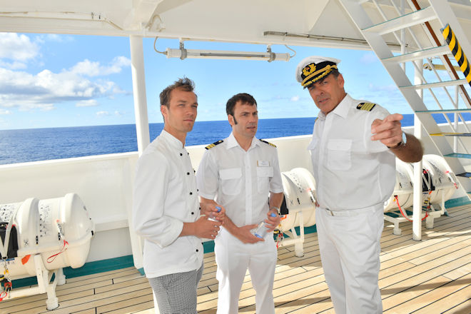 Die Freunde Chief Purser Holger (Daniel Wiemer, M.) und Sous-Chef Thomas (Max Woelky, l.) werden von Kapitän Burger (Sascha Hehn, r.) von der Erpressung unterrichtet.