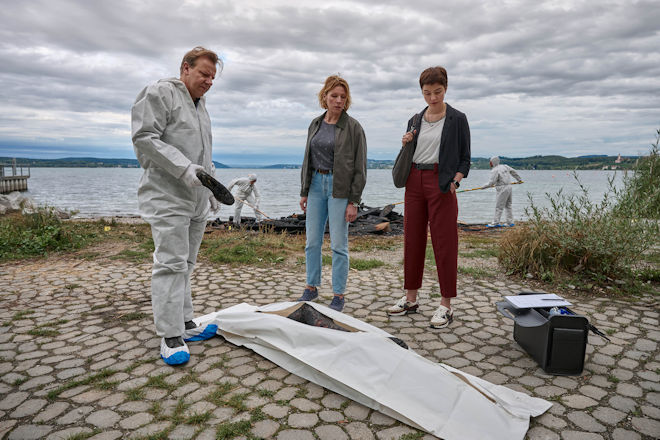 Freitagskrimi "Mordufer - Brennen soll sie": Gerichtsmediziner Gregor Eisen (Ronald Kukulies, l.) gibt den Kriminalkommissarinnen Doro Beitinger (Franziska Weisz, M.) und Chiara Locatelli (Maria W&ouml;rdemann, r.) am Tatort am Ufer des Bodensees erste Informationen zum brisanten Todesfall.