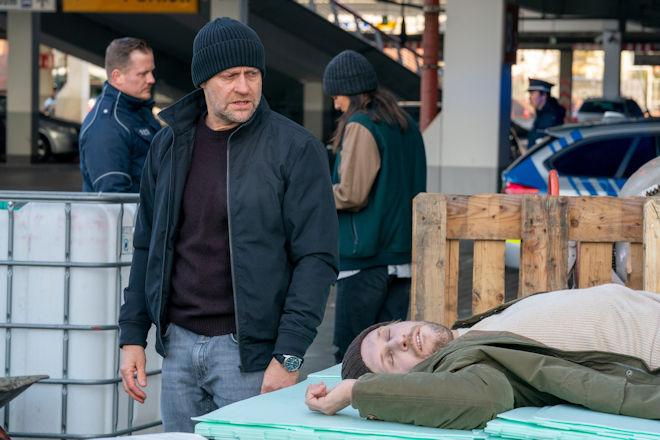 Robert (Jürgen Vogel, 2.v.l.) begutachtet den Tatort und die Leiche von Hannes Seidel (Nils Malten, r.), während Mavi (Aybi Era, 2.v.r.) im Hintergrund mit einem Polizeibeamten spricht.