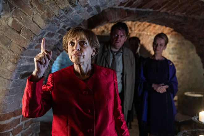 Miss Merkel (Katharina Thalbach, l.) bemerkt durch ihren angefeuchteten Finger einen Luftzug, der auf einen weiteren Geheimgang im Verlies des Schlosses hindeutet, während Kommissar Hannemann (Sascha Nathan, M.) und Katharina von Baugenwitz (Judith Engel, r.) aufmerksam Miss Merkels Treiben verfolgen.