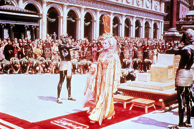 Imperien treffen aufeinander, Ägypten in Rom: Cleopatra (Elizabeth Taylor) ist in Rom angekommen und hat sich von ihrem Thron erhoben, um Caesar und Marcus Antonius zu begrüßen.