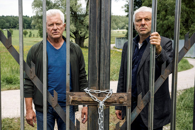 M&uuml;nchen-Tatort "Freies Land": Die Kriminalhauptkommissare Ivo Batic (Miroslav Nemec, l.) und Franz Leitmayr (Udo Wachtveitl, r.) stehen vor dem verschlossenen Eingangstor zum "Freiland"-Gel&auml;nde.