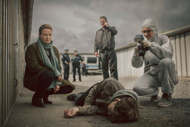 Dr. Theresa Wolff (Nina Gummich, l.), Bruno Lewandowski (Aurel Manthei, M.) und die Spurensicherung (Komparsin, r.) verschaffen sich einen Eindruck von dem Tatort und der Leiche (Philip Günsch, liegend).