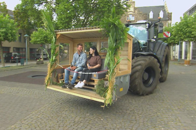 Mit einem Trecker, auf dessen Korb eine kleine Holzhütte aufgebaut ist, fährt Michi zum Bahnhof, um seine Valentina (23) abzuholen.