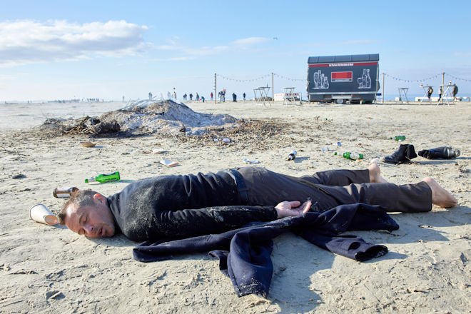 Der Morgen nach der Hochzeit. Der letzte Gast, Rupert (Barnaby Metschurat), hat es nicht nach Hause geschafft und liegt schlafend am Strand neben dem abgebrannten Osterfeuer.