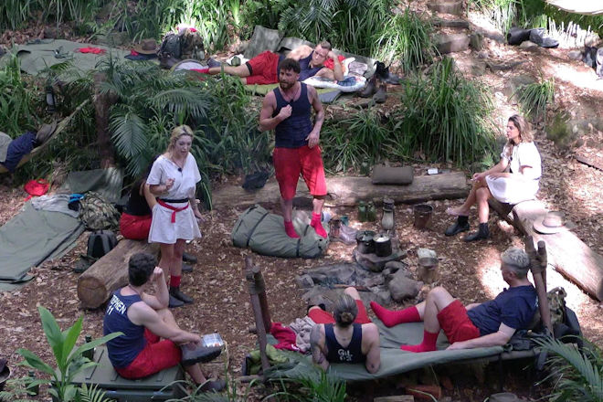 RTL Dschungelcamp 2026: Ariel und Umut Tekin stehen mitten im Camp und reden gleichzeitig aufeinander ein.